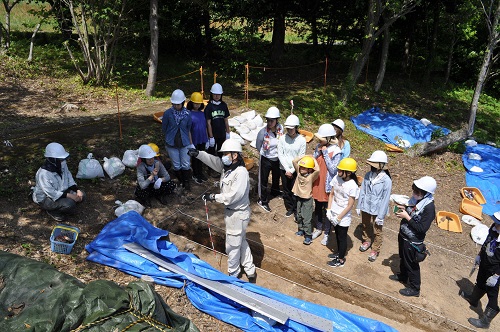 発掘担当の職員の解説を聞く部員たち