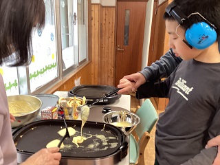 ホットプレートにホットケーキの生地を落とす児童の写真