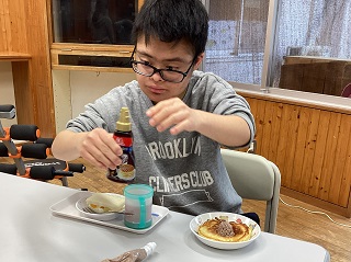 ホットケーキにチョコレートシロップを掛ける児童の写真