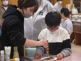 チョコソースをかけてもらう児童と職員